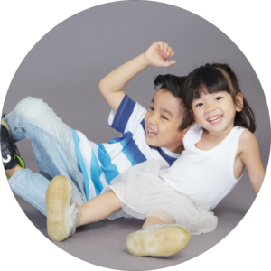 A young brother and sister pose on a grey background